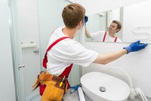 das Arbeiter installiert das Spiegel im das Badezimmer foto