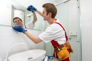 männlich Handwerker hängt das modern elektronisch Badezimmer Spiegel. Zubehör und Möbel zum Badezimmer und Häuser foto