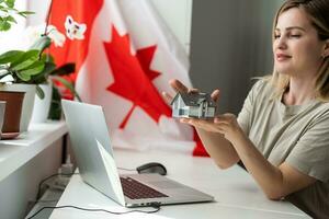 ein weiblich Hand hält ein klein Kanada Flagge und ein Laptop auf das Hintergrund von das Universität. schließen oben foto