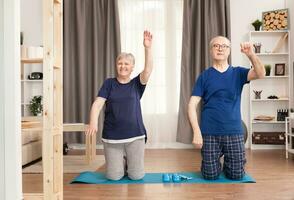 glücklich alt Ehefrau ausüben in der Nähe von ihr Ehemann. alt Person gesund Lebensstil Übung beim heim, trainieren und Ausbildung, Sport Aktivität beim Zuhause auf Yoga Matte. foto