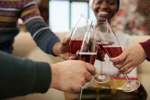 heiter Kollegen halten Getränk Brille und Klirren während feiern Winter saisonal Urlaub zusammen. Unternehmen Arbeitskräfte Trinken funkelnd Wein beim Weihnachten korporativ Party foto