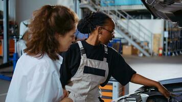 trainiert Handwerker im Garage Arbeitsplatz Festsetzung Auto zum Kunde, gründlich Überprüfung unterhalb Fahrzeug Haube. afrikanisch amerikanisch Experte tun jährlich Instandhaltung auf Klient Automobil im Auto Reparatur Geschäft foto