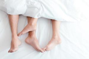 Nahaufnahme Füße des Paares auf dem Bett. Liebhaber von Mann und Frau lieben sich unter der Decke oder dem Bettlaken. Sex im Urlaub Thema. Valentinstag und Flitterwochen-Konzept