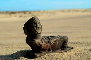 ein Statue von ein Mann Sitzung auf das Sand foto