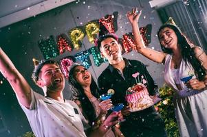 Asiatische Freunde, die Spaß an der Geburtstagsfeier im Nachtclub mit Geburtstagskuchen haben. Event- und Jubiläumskonzept. Menschen Lebensstil und Freundschaft foto