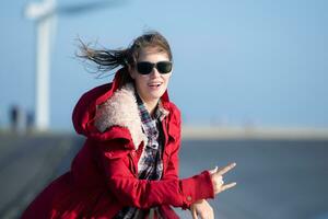 auf das Hintergrund von Windmühlen, ein jung Frau im ein rot Jacke ist genießen ihr Winter Urlaub. foto