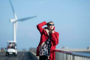 auf das Hintergrund von Windmühlen, ein jung Frau im ein rot Jacke ist genießen ihr Winter Urlaub. foto