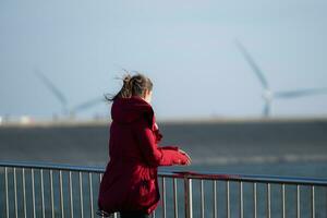 auf das Hintergrund von Windmühlen, ein jung Frau im ein rot Jacke ist genießen ihr Winter Urlaub. foto