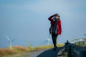 auf das Hintergrund von Windmühlen, ein jung Frau im ein rot Jacke ist genießen ihr Winter Urlaub. foto