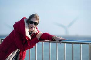 auf das Hintergrund von Windmühlen, ein jung Frau im ein rot Jacke ist genießen ihr Winter Urlaub. foto