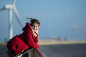 auf das Hintergrund von Windmühlen, ein jung Frau im ein rot Jacke ist genießen ihr Winter Urlaub. foto