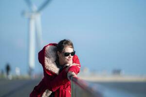 auf das Hintergrund von Windmühlen, ein jung Frau im ein rot Jacke ist genießen ihr Winter Urlaub. foto