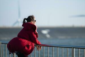 auf das Hintergrund von Windmühlen, ein jung Frau im ein rot Jacke ist genießen ihr Winter Urlaub. foto