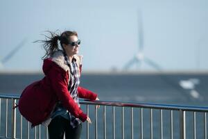auf das Hintergrund von Windmühlen, ein jung Frau im ein rot Jacke ist genießen ihr Winter Urlaub. foto