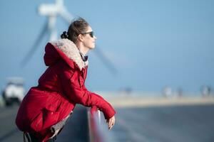 auf das Hintergrund von Windmühlen, ein jung Frau im ein rot Jacke ist genießen ihr Winter Urlaub. foto