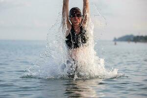 Frau Schwimmer springen aus von Meer Wasser Wasser mit Streaming Spritzer. foto