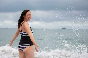 reifen glücklich Frau im ein Badeanzug genießt das Meer und das Brise von das Welle auf ein Sommer- Tag. foto