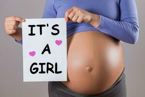 Bild von schließen oben Bauch von schwanger Frau halten Papier mit Text es ist ein Mädchen auf grau Hintergrund. foto