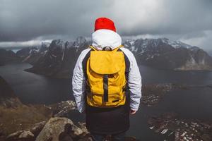 Reisender Mann mit gelbem Rucksack, der auf Felsen vor dem Hintergrund von Meer und Bergen steht foto