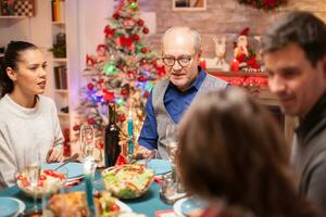 glücklich Senior Mann beim das Kopf von das Tabelle beim Weihnachten Familie Abendessen mit köstlich Lebensmittel. foto