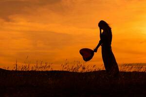 Silhouette von ein traurig Frau halten Herz geformt Ballon beim das Sonnenuntergang. foto