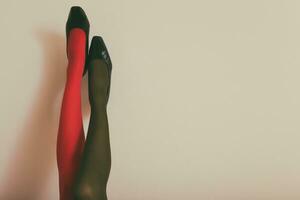 schön Beine von ein Frau im im anders Farbe Strumpfhose und hoch Absätze oben im Vorderseite von wandgetönt Foto