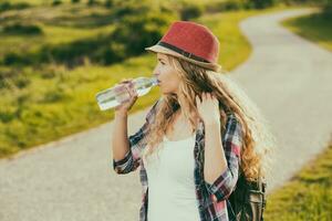 schön jung Frau Trinken Wasser während ruhen von Gehen beim das Land Straße. foto