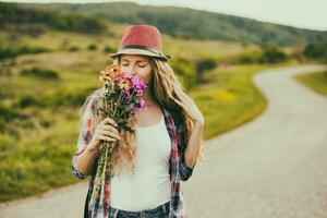 schön jung Frau genießt riechen Strauß von Blumen beim das Land Straßenton Bild. foto