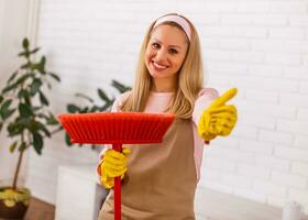 schön Hausfrau zeigen Daumen oben während genießt Reinigung ihr heim. foto