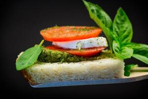 frisch Scheibe von Brot mit Pesto Soße, Mozzarella und Tomate auf ein hölzern Spatel mit Basilikum. foto