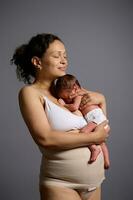 herrlich gemischt Rennen Frau, glücklich liebend Pflege Mutter umarmen ihr Neugeborene Baby, Stehen zusammen isoliert auf grau foto