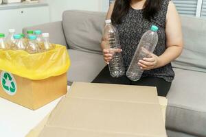 Zuhause recyceln Öko Grün Null Konzept Frau werfen leeren Plastik Flasche im Recycling Behälter mit Gelb Müll Taschen beim heim. foto