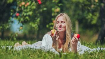 ein jung Frau ist Lügen auf das Gras im das Garten Essen ein Apfel. foto