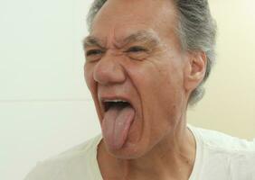 älter reifen Mann kleben seine Zunge aus Prüfung es im Vorderseite von ein Spiegel foto