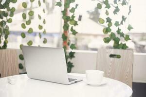 Laptop mit spotten oben leer Bildschirm auf hölzern Tabelle im Vorderseite von Kaffee Geschäft Cafe Raum zum Text. Produkt Anzeige Montage- Technologie Konzept. foto