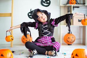 Porträt eines kleinen Mädchens mit Hexenkleid spielt im Zimmer, das im Halloween-Festival dekoriert ist foto