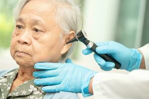 Audiologe oder ent Arzt verwenden Otoskop Überprüfung Ohr von asiatisch Senior Frau geduldig Behandlung Hören Verlust Problem. foto