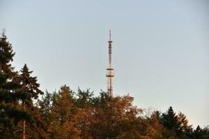 ein Fernsehen Turm auf das Hintergrund von Herbst Bäume. ein Eisen hoch Struktur im das Stadt. foto