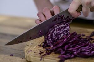 Hacken rot Kohl mit ein Küche Messer auf ein hölzern Schneiden Tafel foto