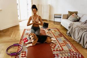 Schwarze junge Frau, die während der Yogapraxis mit ihrem Hund meditiert