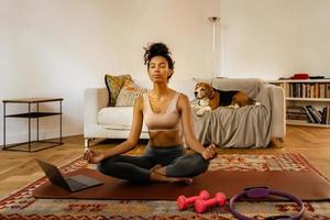 Schwarze junge Frau, die während der Yogapraxis mit ihrem Hund meditiert foto