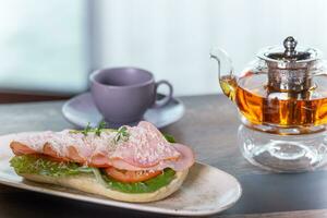 ein Licht hausgemacht Frühstück bestehend aus von ein Tasse von schwarz Tee und ein frisch Schinken Sandwich. foto