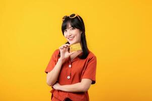 Porträt jung schön asiatisch Frau glücklich Lächeln gekleidet im Orange Kleider zeigen Anerkennung Karte isoliert auf Gelb Hintergrund. Zahlen und Kauf Einkaufen Zahlung Konzept. foto