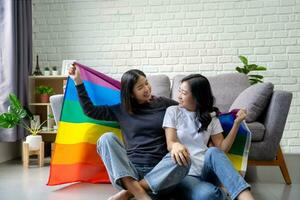 lgbt Paar, jung asiatisch Frau umarmen jeder andere unter Regenbogen Flaggen im Leben Zimmer foto