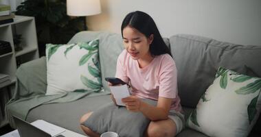 Porträt von jung asiatisch Frau halten Papier verschiedene Aufwand Rechnungen und Pläne zum persönlich Finanzen und mit Taschenrechner auf Smartphone Berechnung Einkommen und Kosten beim Zu Hause zu Hause Finanzen foto