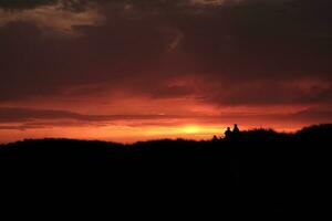 Silhouette von Menschen Stehen auf oben von das Dünen beim Sonnenuntergang foto