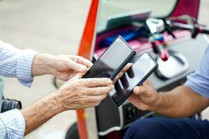 Nahansicht und Ernte Hände von Senior Tourist bezahlen das Fahrpreis zu das Tuk Tuk Thailand Taxi Treiber durch Clever Telefon. foto