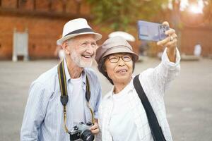 Nahansicht amerikanisch Senior Tourist Mann mit seine Tour leiten nehmen ein Foto Selfie auf verschwommen von Stadt Tor Hintergrund. Senior Tourist Konzept