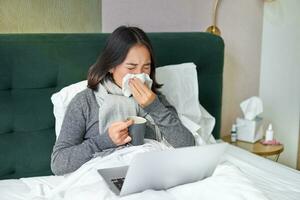 Frau mit kalt, haben Grippe, bleiben im Bett, Niesen im Serviette, flüssig Nase und Grippe Symptome foto