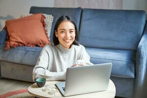 Arbeit von heim, freiberuflich und E-Learning Konzept. jung Frau studieren, Sitzung im Vorderseite von Laptop, Arbeiten auf Fernbedienung, Arbeitsplatz im Leben Zimmer foto